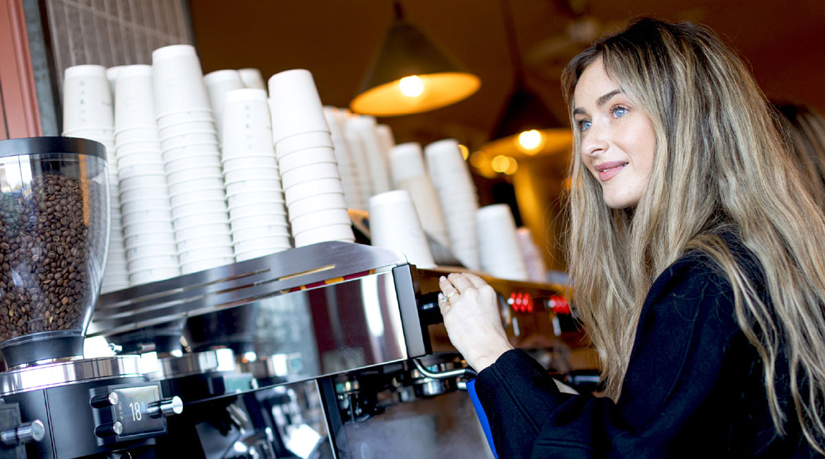 Radharc caifé - barista ag tabhairt faoi mheaisín caife a oibriú