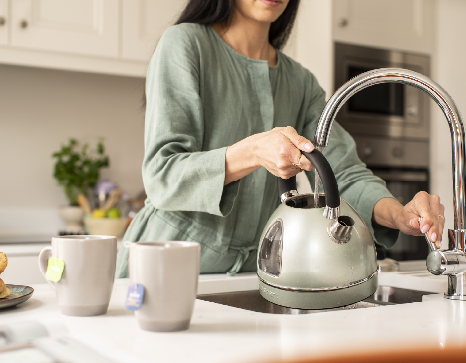 Home kitchen environment with a close up of kettle being filled from a tap.