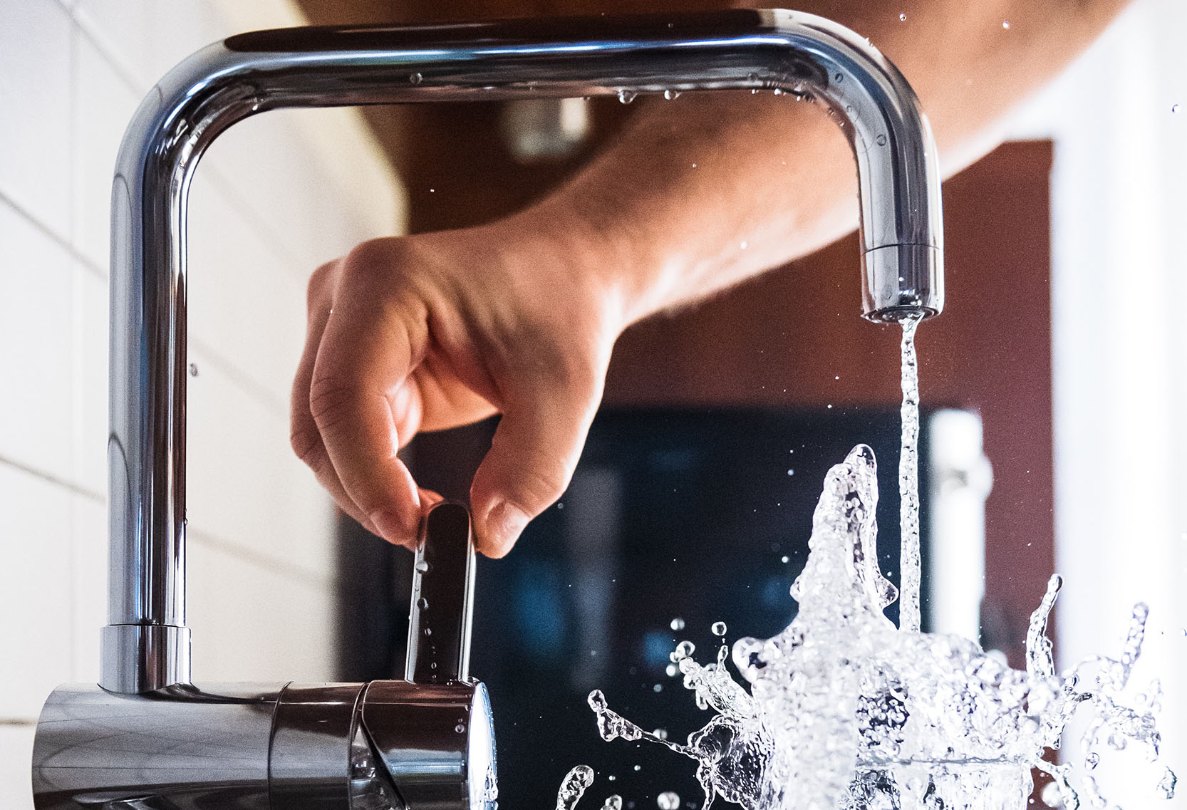 A person turning off a tap with running water splashing in the sink