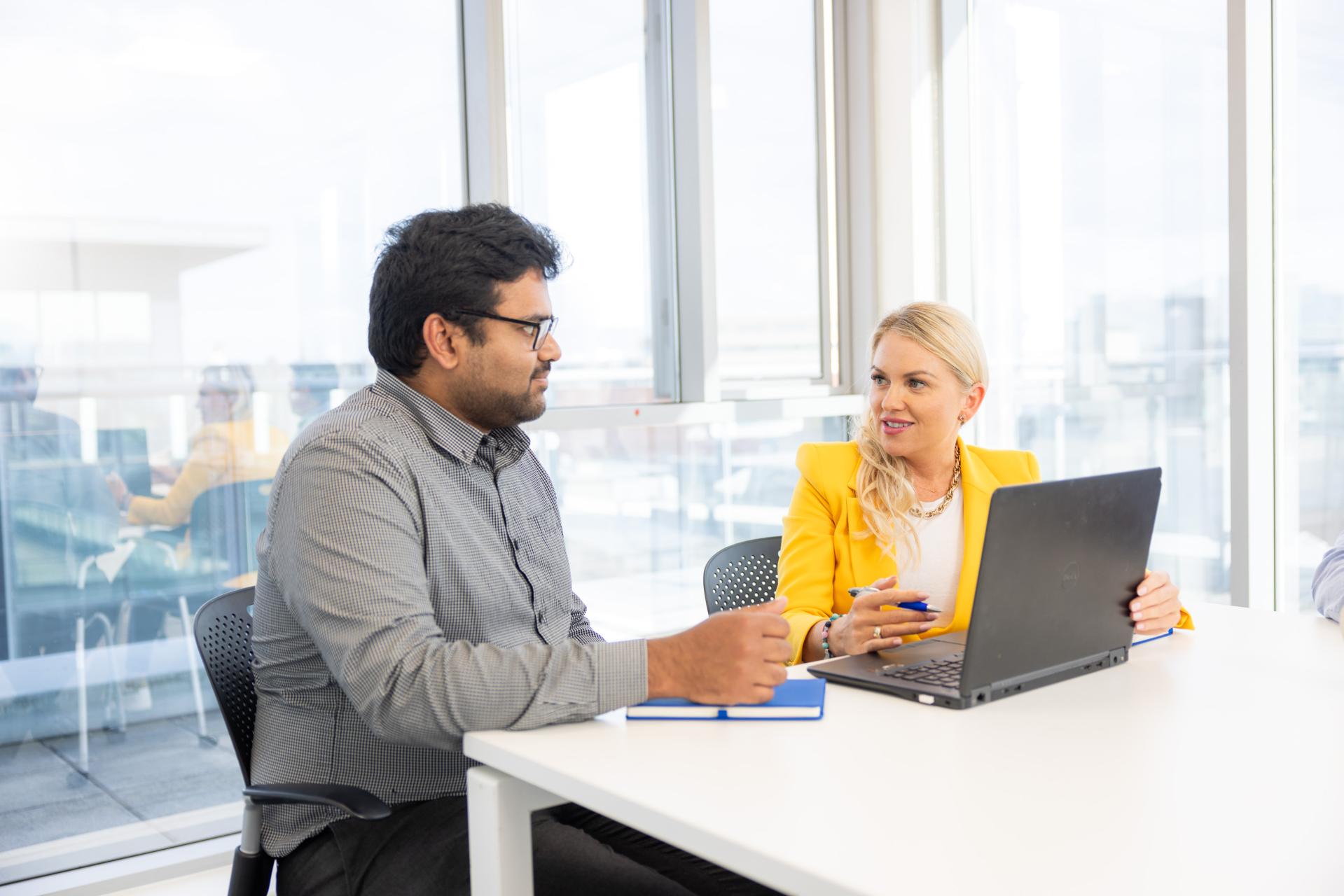 A man and woman talking over a laptop within a office