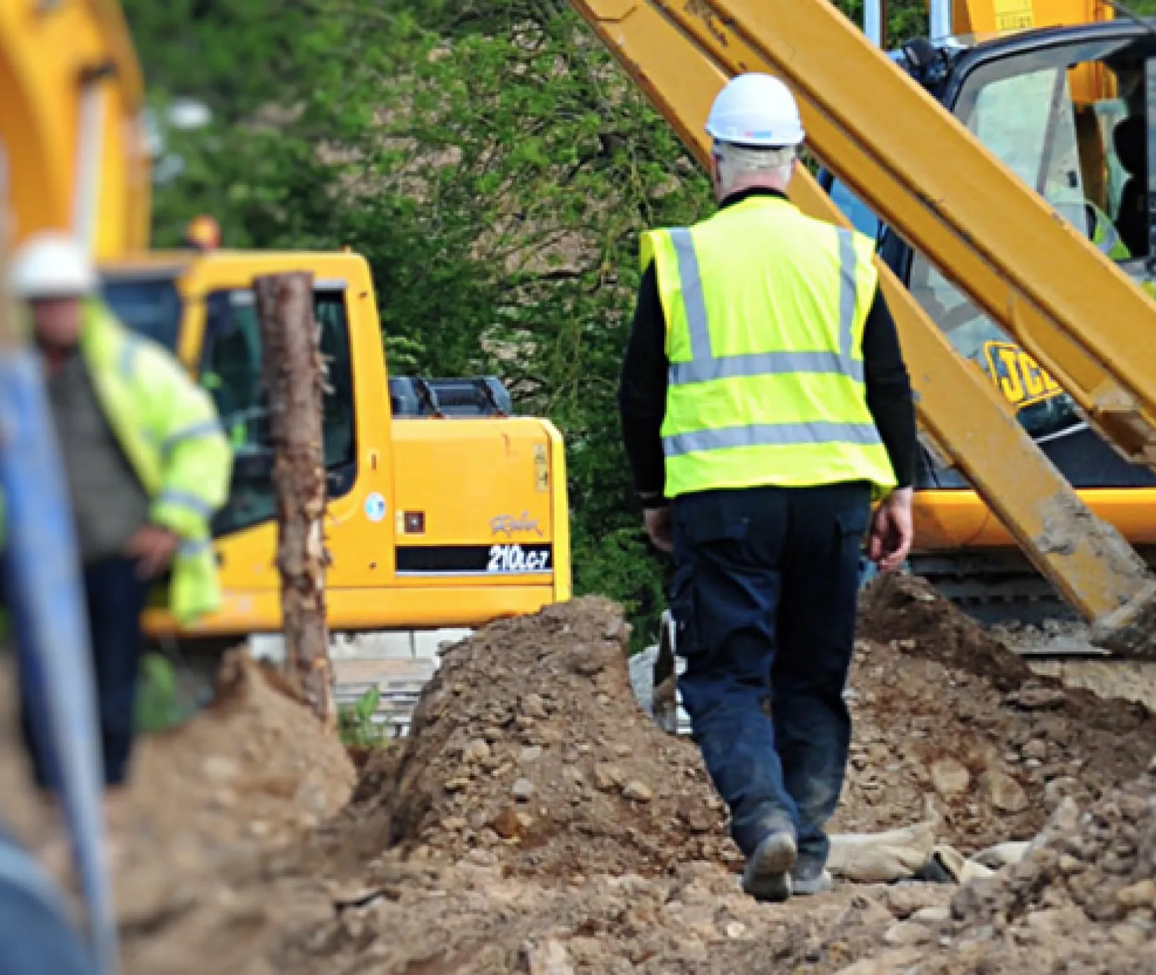 A worker walking through the construction site surrounded by diggers and muck