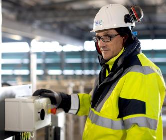 A UÉ worker standing by a red start / stop button in a industrial unit