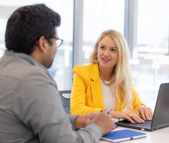 A woman in a yellow jacket speaking to another employee in a meeting