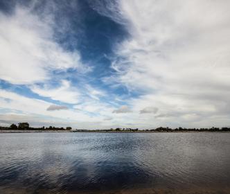 A large lake with a cloudy sky in front of a field