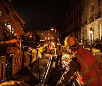 Workers laying pipe using a crane during nighttime
