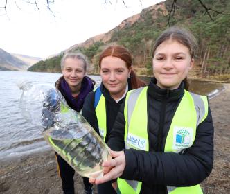 Three kids by a like holding a large plastic bottle of water