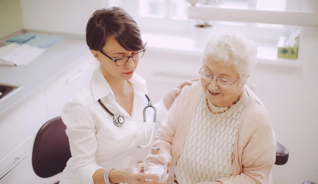 A doctor handing an elderly woman a glass of water